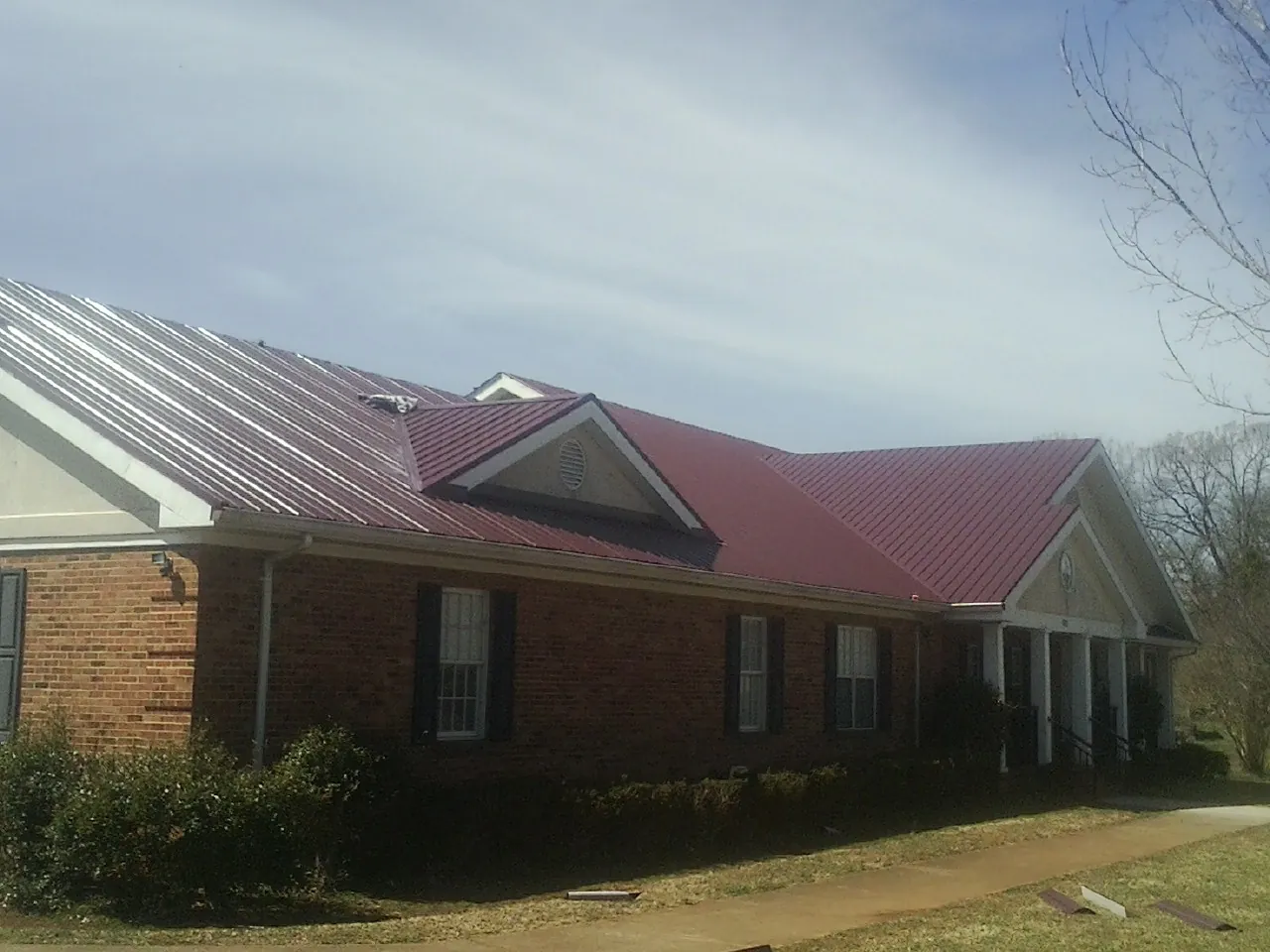 Red metal roof with gabled entries on a long brick building, from a Hail Damage Roof Repair job in Roslyn