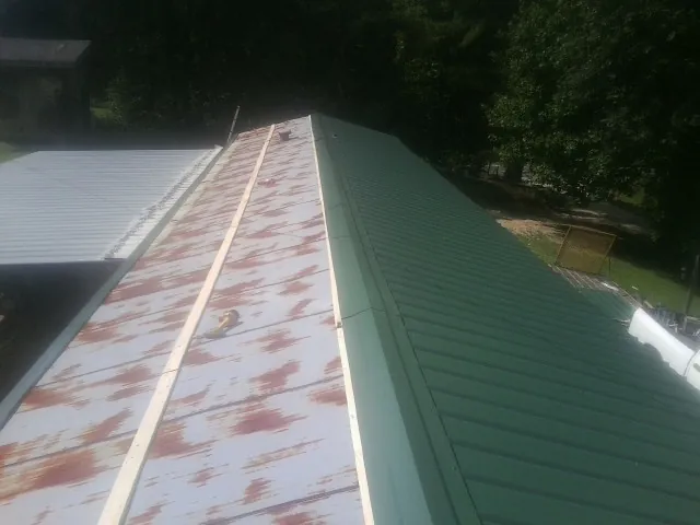 Old rusted panels beside newly installed green metal roofing — Wind Damage Roof Repair by Roofing Brothers in Roslyn