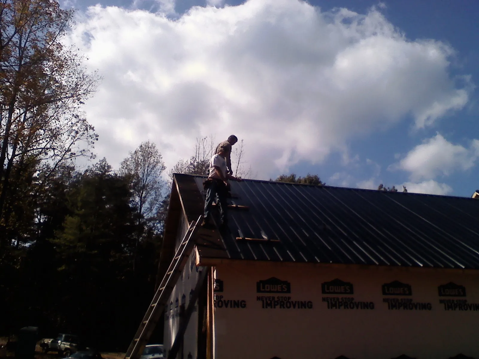 Roofer fastening dark metal panels high against a cloudy sky, from a Roof Inspection job in Roslyn